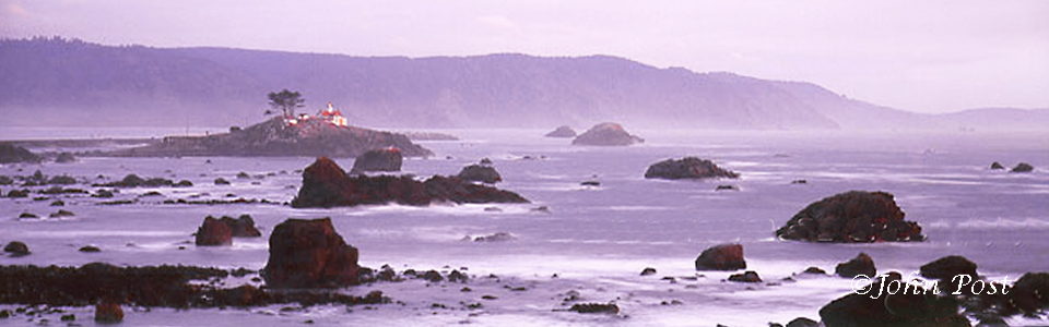 View across rocks and water to Crescent City Lighthouse, coastal mountains in background