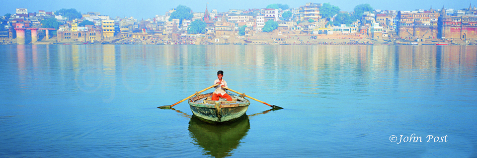 India,  young boy on boat facing camera, city waterfront of Varanasi in background