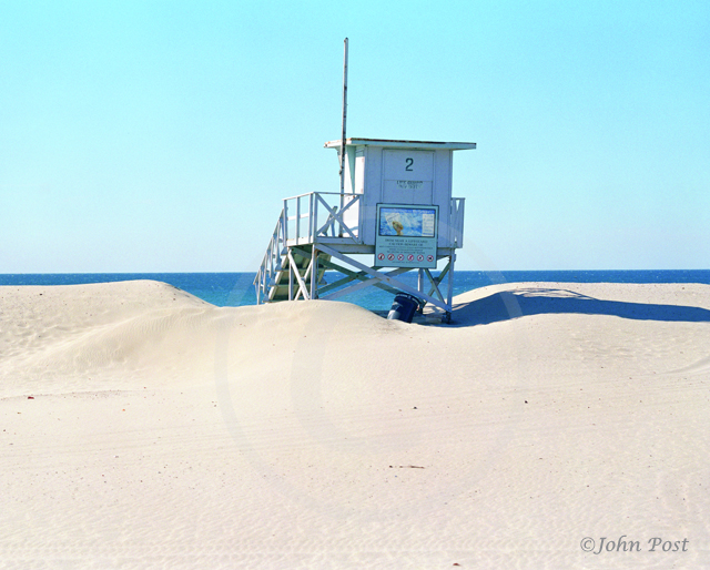 Lifeguard tower on beach, clear  sky with volleyball net and seagull on top of pole.
