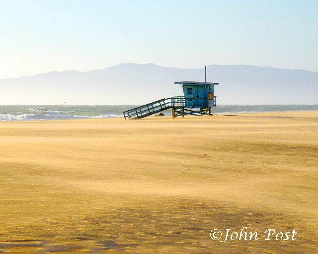 Lifeguard tower on beach, clear sunset sky with volleyball net and seagull on top of pole.